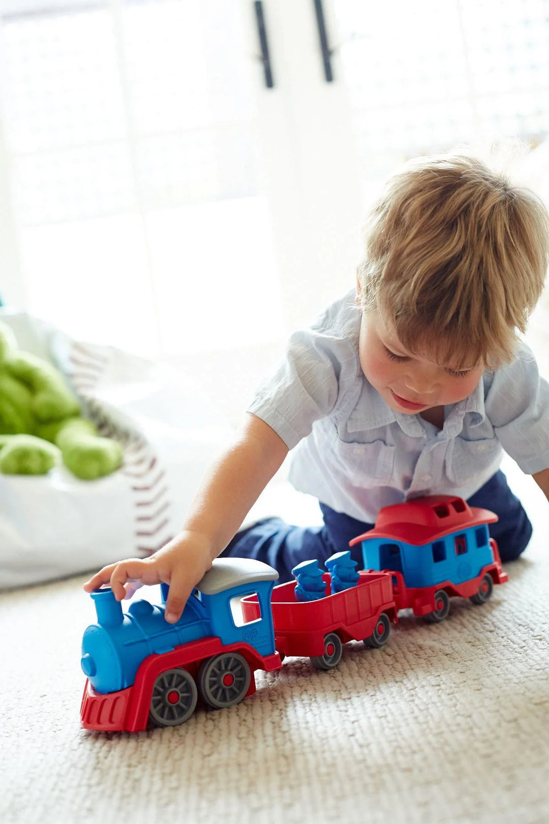 Child playing with a toy train set on a light-colored floor.