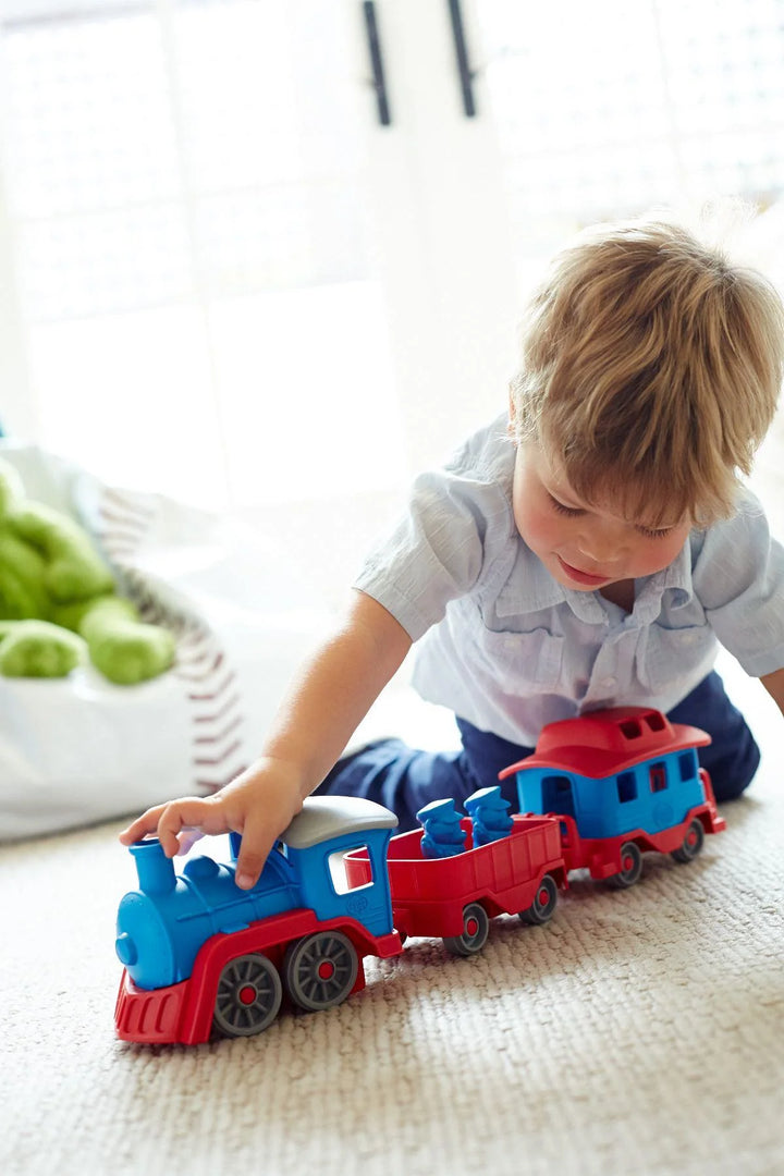 Child playing with a toy train set on a light-colored floor.