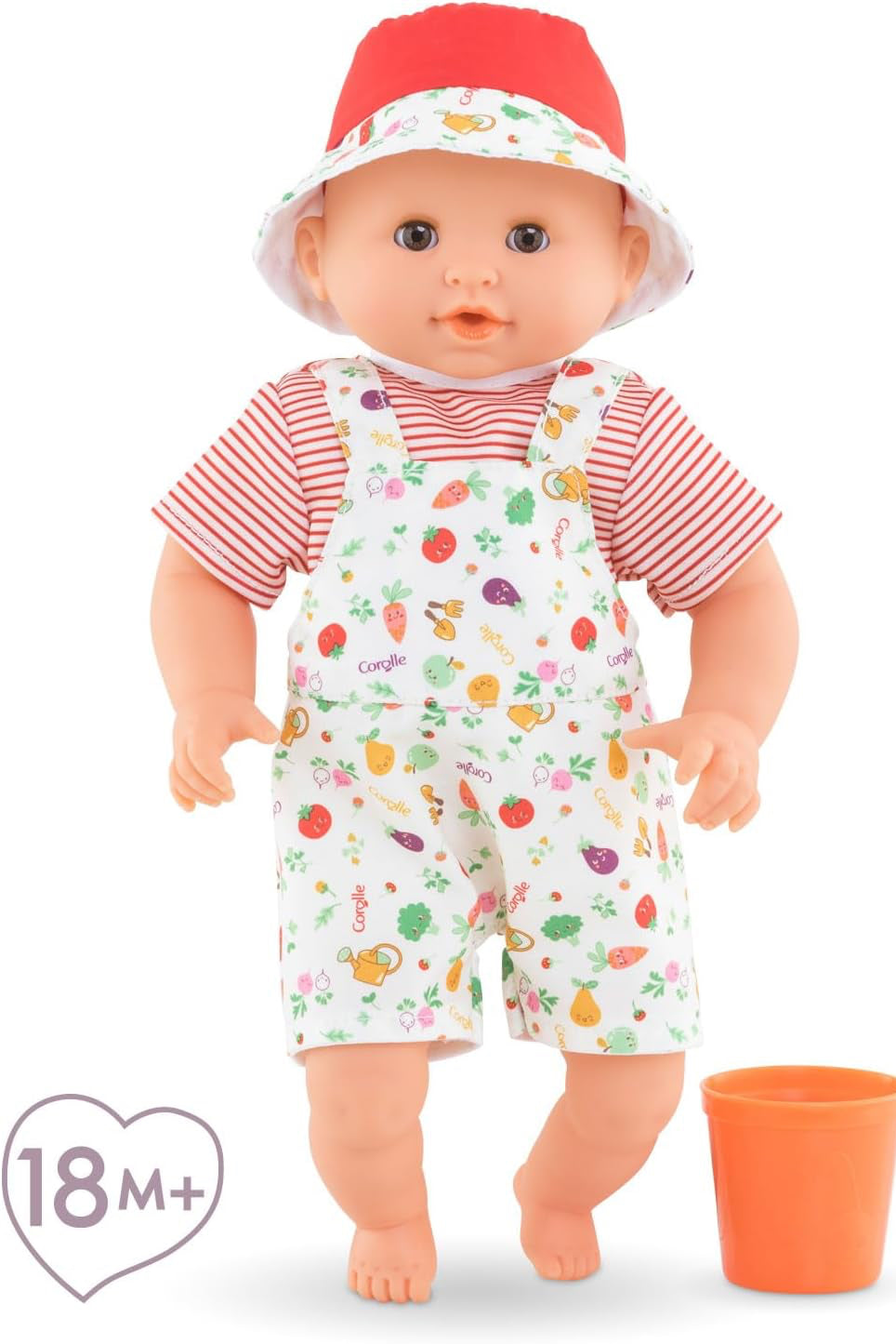 Baby doll with red hat and fruit-patterned outfit next to an orange cup on a white background