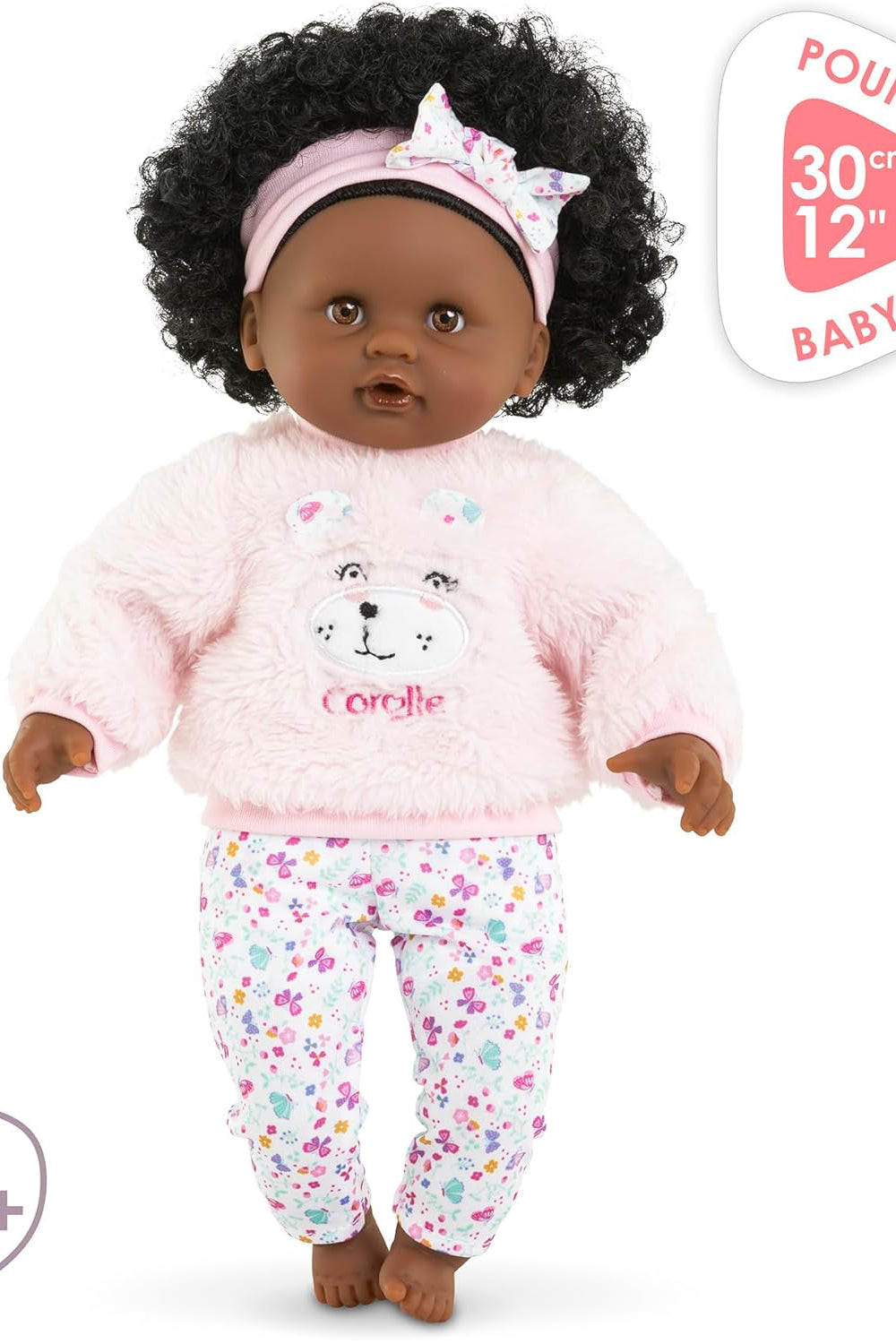 Baby doll in pink outfit with teddy bear design, standing against a white background.