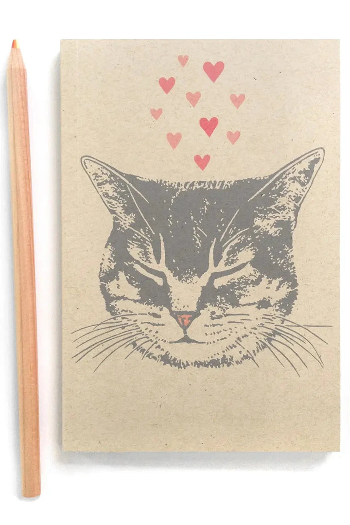 Notebook with a cat illustration and pink hearts, accompanied by a pencil on a white background 