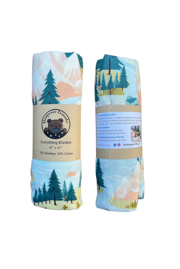 Two folded blankets with a forest design and brand label on a white background
