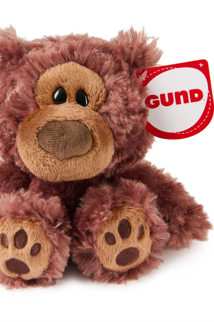 Photo of stuffed animal bear with a tag on the ear, with "gund" written in red 