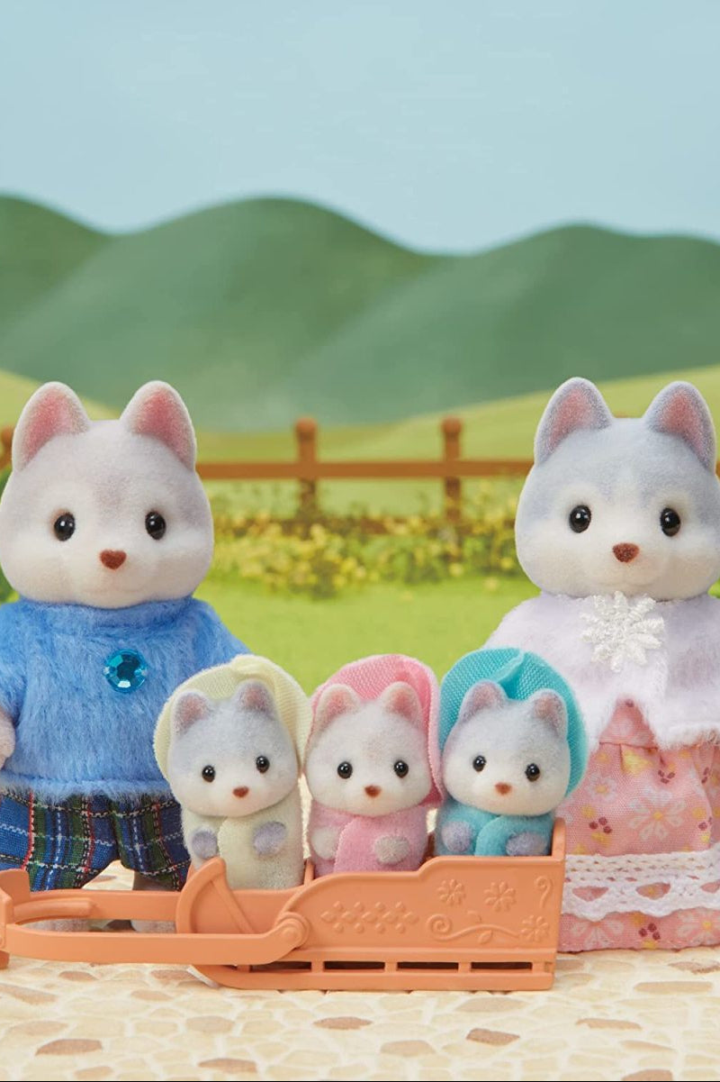 A pastural scene with toy hucky family including a mother, father, and triplet babies in a sled. Clothing is cozy. 