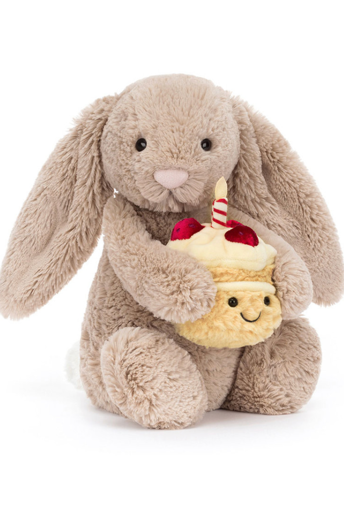 Photo of beige stuffed bunny with floppy ears and birthday cake with single candle and strawberries on top