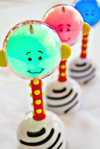 A colorful NogginStick light-up rattle with a smiling face, held by a baby.